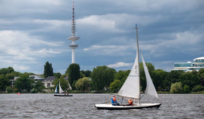 Dunkle Wolken ziehen über den Fernsehturm und die Außenalster, auf der Segelboote kreuzen.