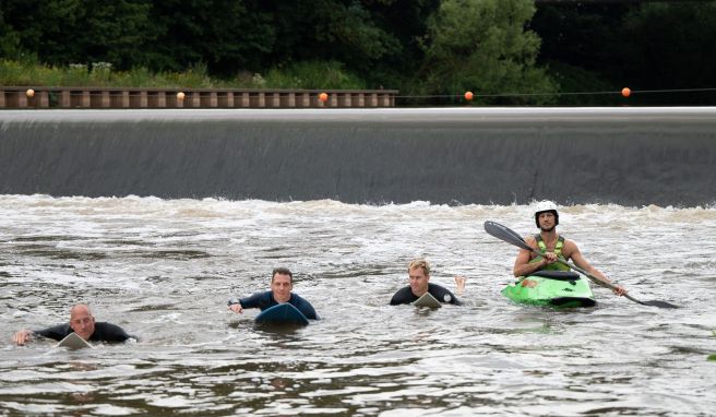 Surfer und ein Kayakfahrer fahren an dem Wehr, an dem die Surfwelle entstehen soll. 