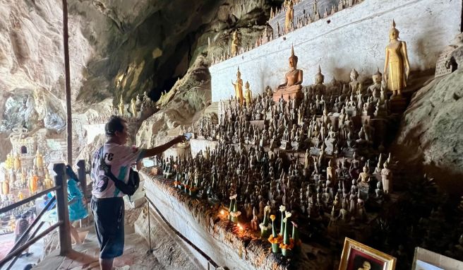 Ein Mann besprenkelt Buddha-Statuen in den Pak Ou Caves als Zeichen des tiefen Respekts mit Wasser.