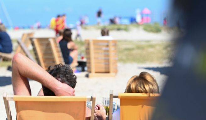 Zwei Gäste der Beachbar am Naturstrandt genießen den Blick auf die Nordsee bei einem Kaltgetränk.