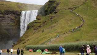 Touristen spazieren am Wasserfall Skogafoss vorbei Touristen spazieren am Wasserfall Skogafoss vorbei