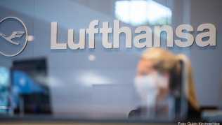 Eine Mitarbeiterin der Lufthansa sitzt mit ihrer Mund- und Nasenschutzmaske am Check-in im Flughafen Münster-Osnabrück Eine Mitarbeiterin der Lufthansa sitzt mit ihrer Mund- und Nasenschutzmaske am Check-in im Flughafen Münster-Osnabrück