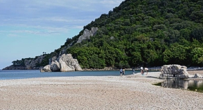 Selbst im Sand am Strand stehen noch ein paar alte Mauerreste. Doch hier lockt vor allem die weite Bucht mit leuchtend blauem Wasser.