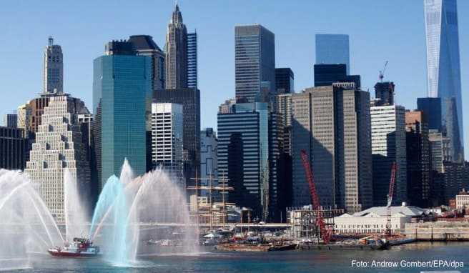 Ein Feuerwehrboot verspritzt Wasser in bunten Farben auf dem East River vor der Skyline von Lower Manhattan. Die Downtown Alliance sucht für die Südspitze Manhattans einen Chef-Entdecker