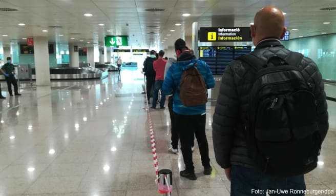 In einer langen Schlange stehen Einreisende aus dem Ausland im Terminal 1 des Flughafens in Barcelona vor der Gesundheitskontrolle zur Temperaturmessung an