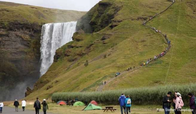 Touristen spazieren am Wasserfall Skogafoss vorbei Touristen spazieren am Wasserfall Skogafoss vorbei