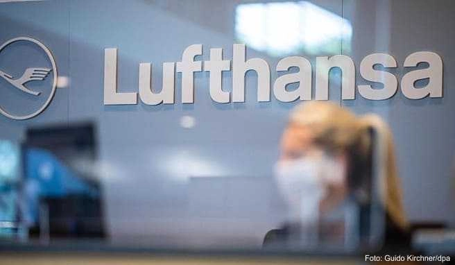 Eine Mitarbeiterin der Lufthansa sitzt mit ihrer Mund- und Nasenschutzmaske am Check-in im Flughafen Münster-Osnabrück