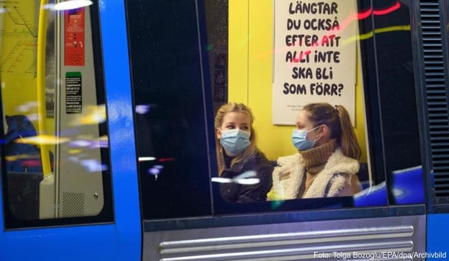 Zwei junge Frauen sitzen mit Mund-Nasen-Schutz in einer U-Bahn